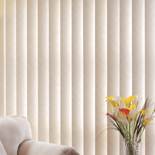 A set of white vertical blinds covering a window with a vase of colorful flowers and a white chair in the foreground.